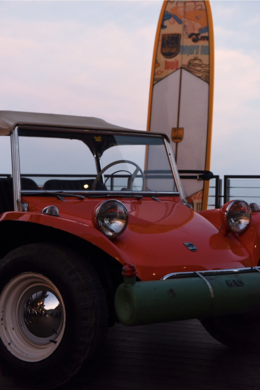 the original Meyers Manx dune-buggy with a surfboard next to it.
