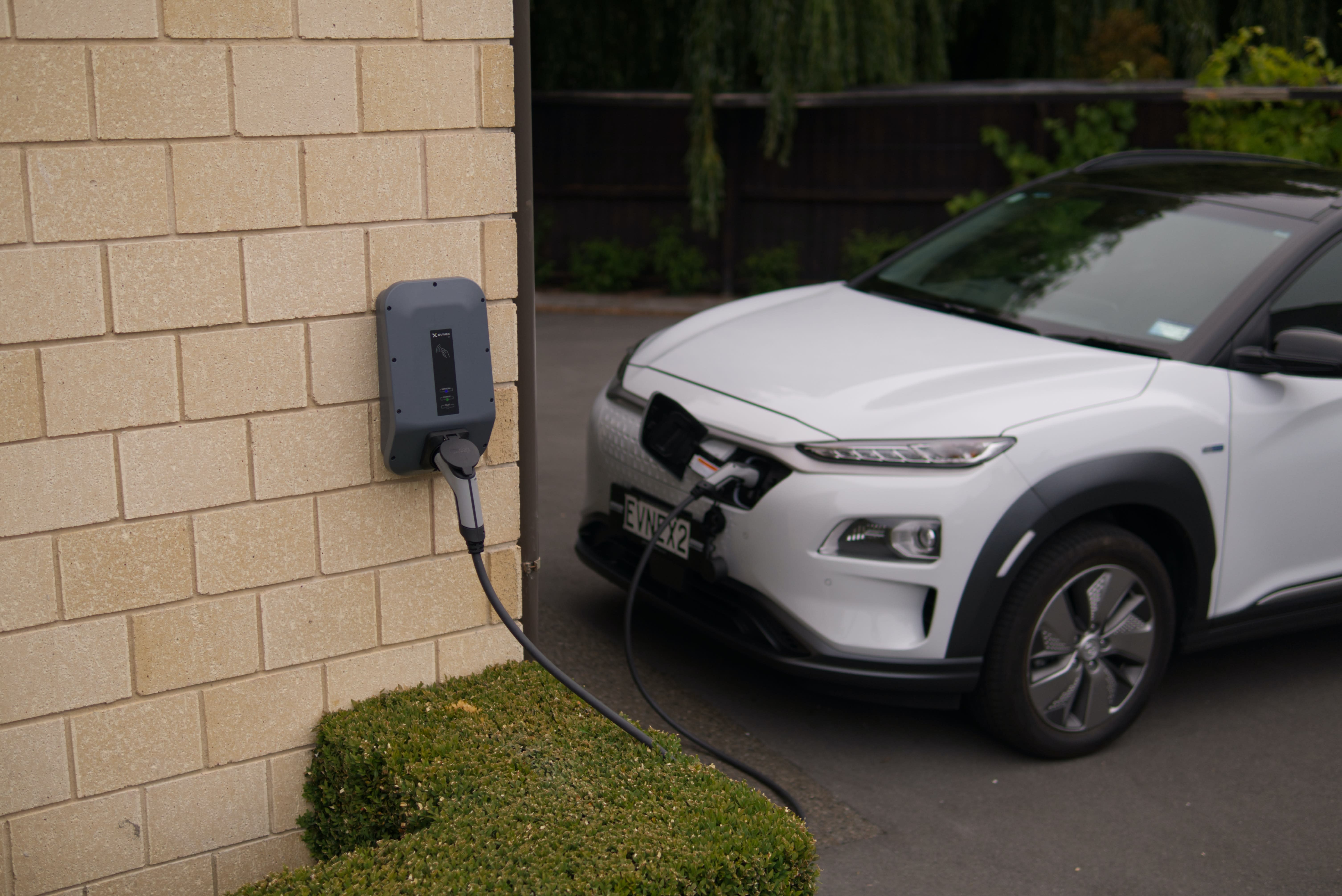 white electric car charging on the driveway of a residence.