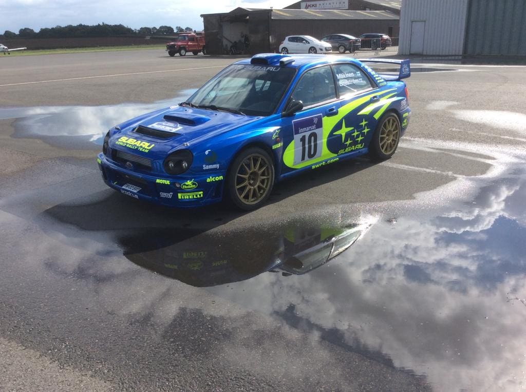 Tommi Mäkinen's blue Subaru rally car on an airport tarmac.