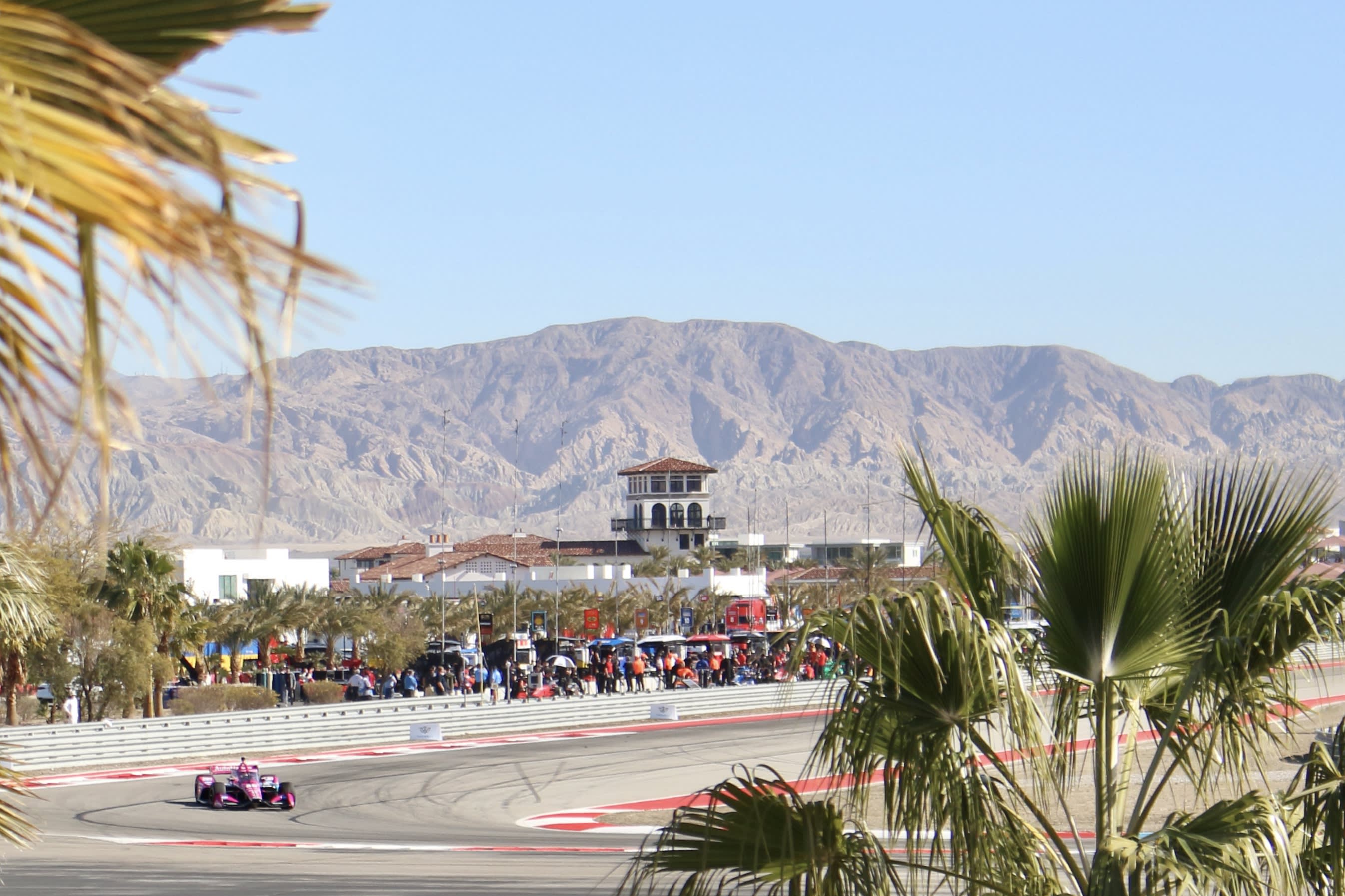 image of a race car on the track at The Thermal Club with palm trees in the foreground and the mountains in the background.