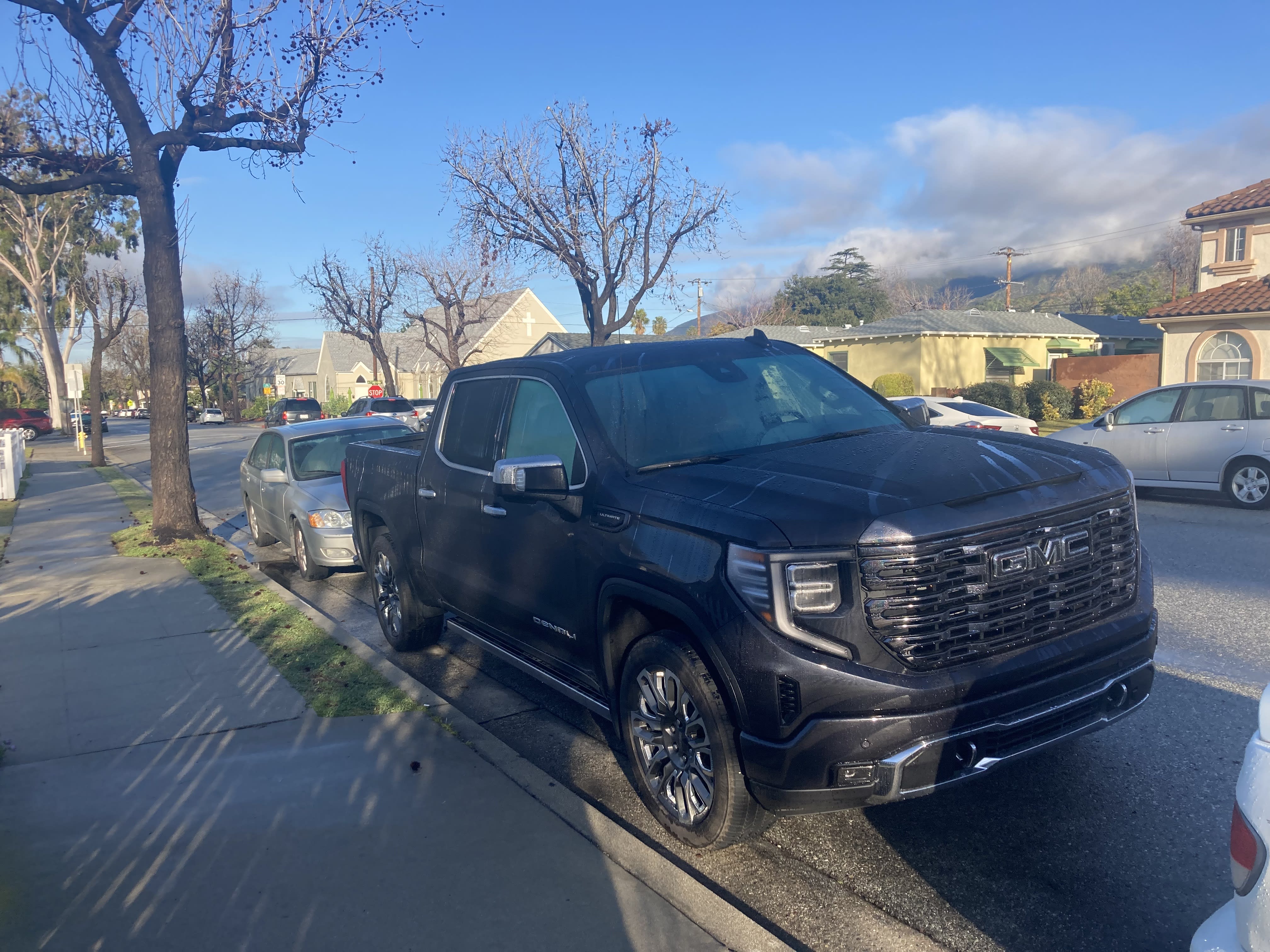a large GMC pickup parked on the street amongst smaller cars