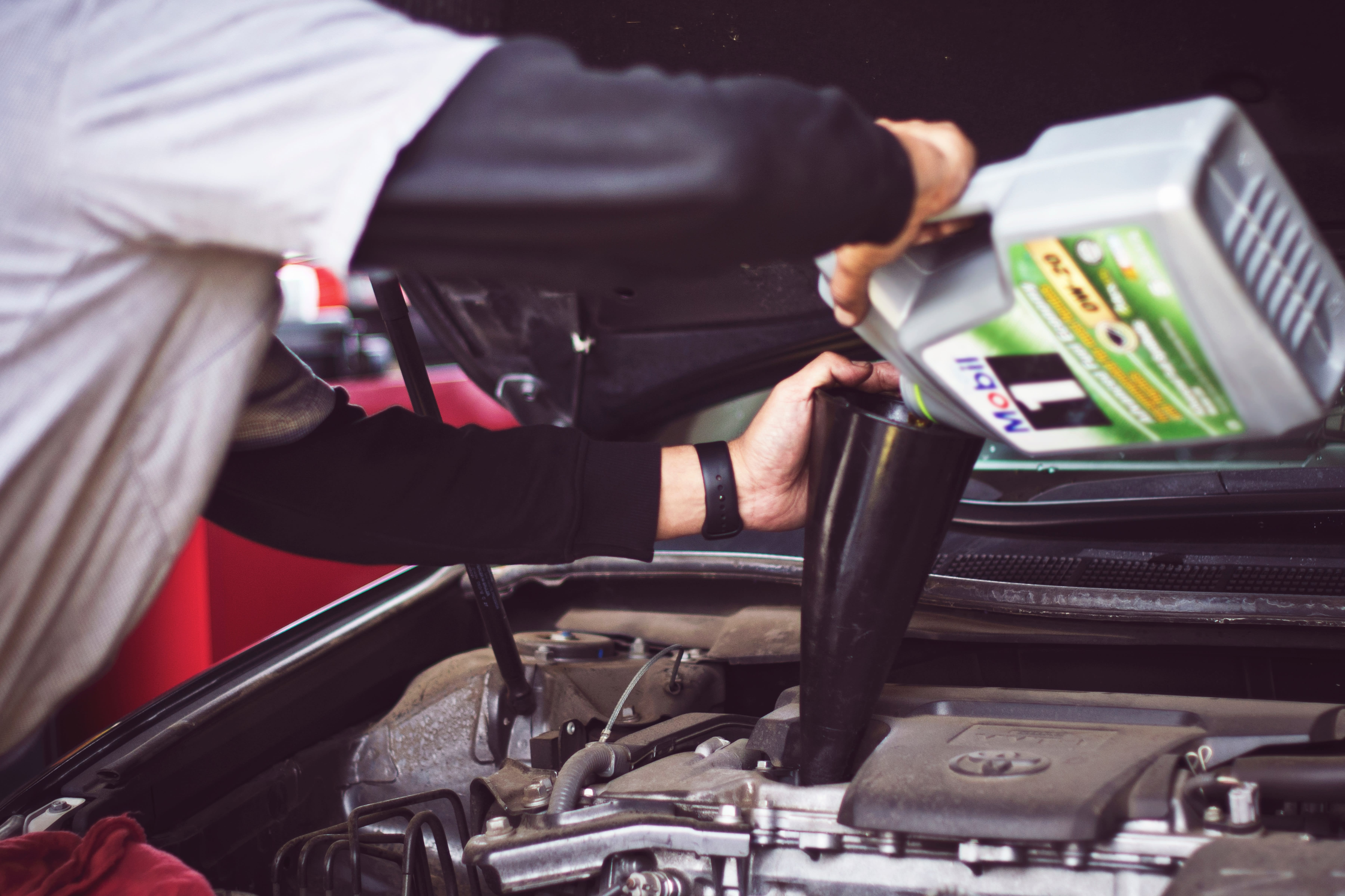 a person filling oil into a car engine