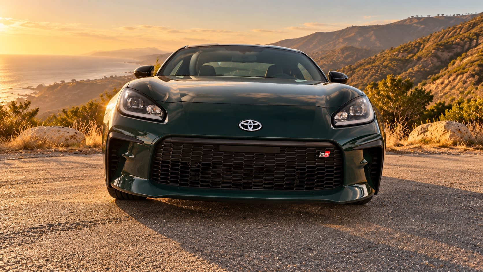 Digitally altered low front view of a green 2025 Toyota GR86, showing its grille and headlights against a generated coastal landscape.