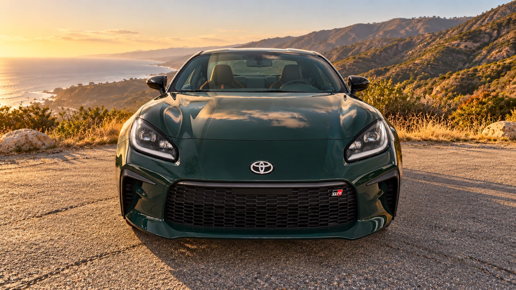 Digitally altered head-on view of a green 2025 Toyota GR86 with generated ocean and hillside scenery.