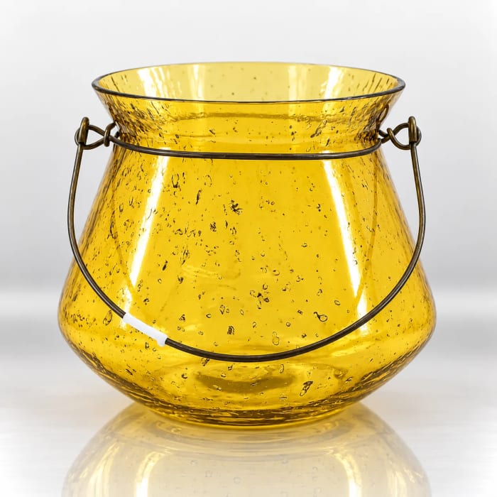 Golden-yellow textured glass candle holder with an antique-bronze metal handle and rounded vessel design.