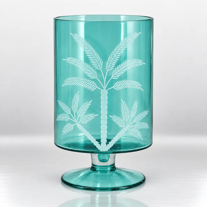 Turquoise glass pedestal candle holder with a white palm tree design.