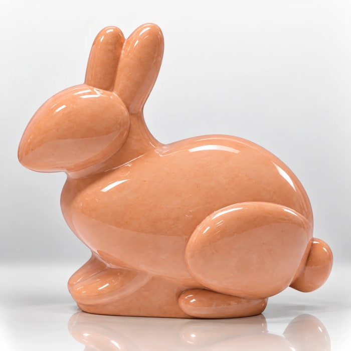 Glossy peach bunny figurine with upright ears, rounded body and sculptural tail.