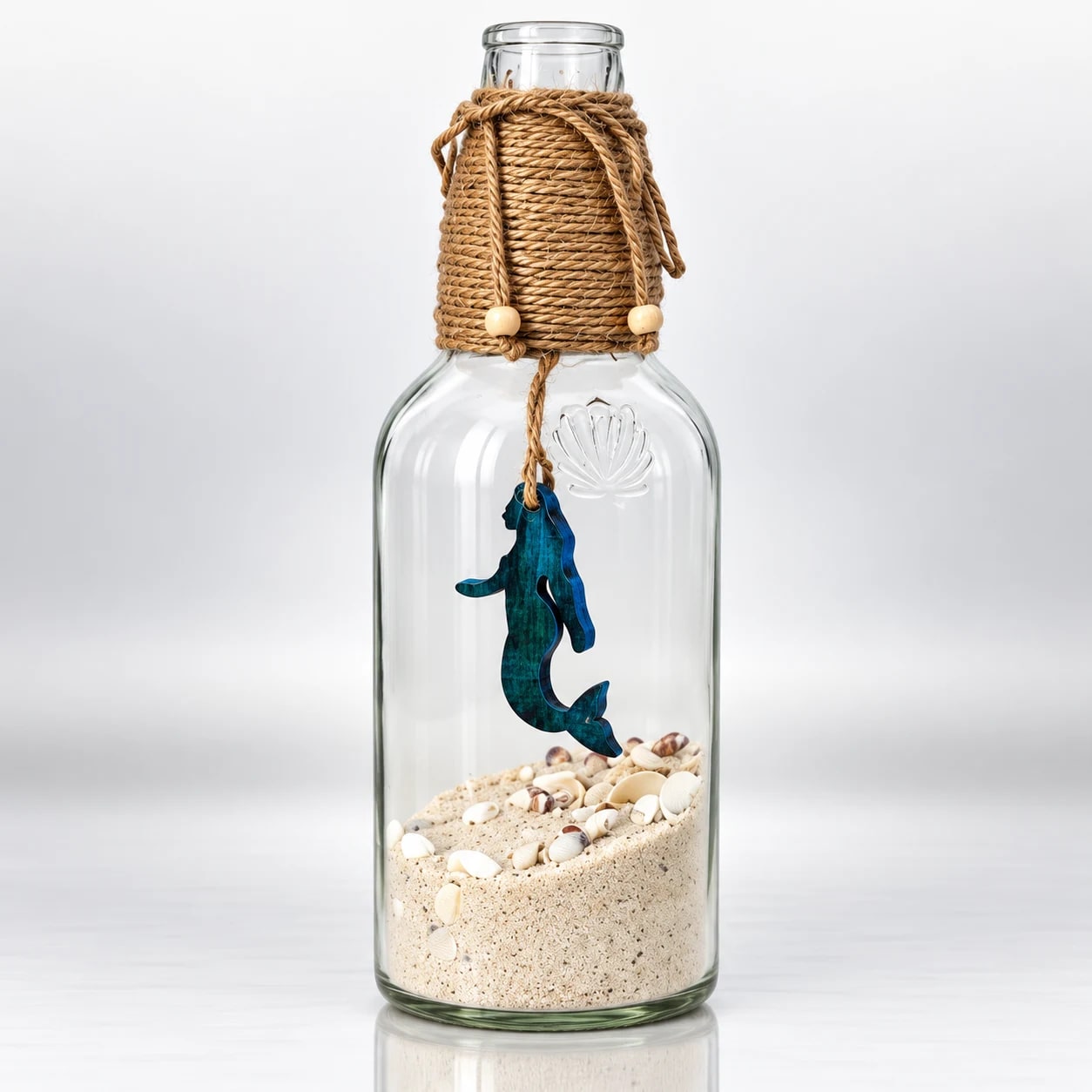 Clear glass bottle with blue seahorse, sand, seashells and woven jute rope