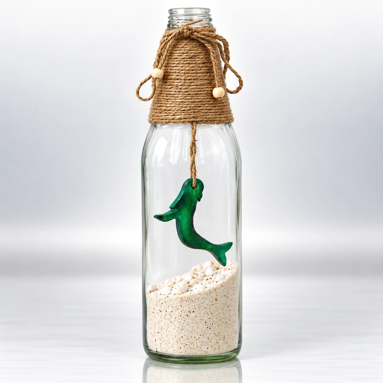Clear glass bottle with green dolphin, sand, seashells and woven jute rope