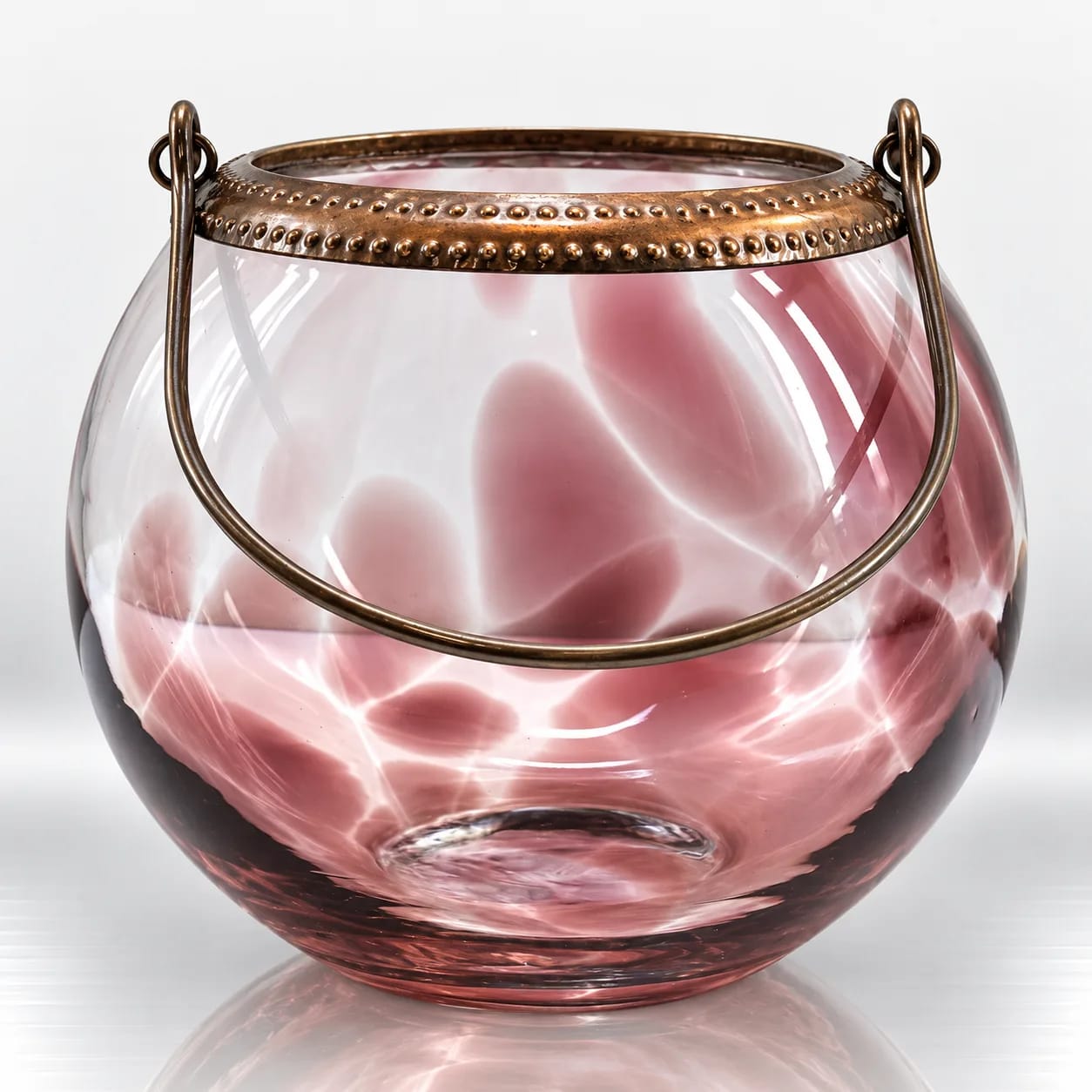 Rose pink rounded glass candle holder with antique bronze-tone decorative rim and curved metal handle.