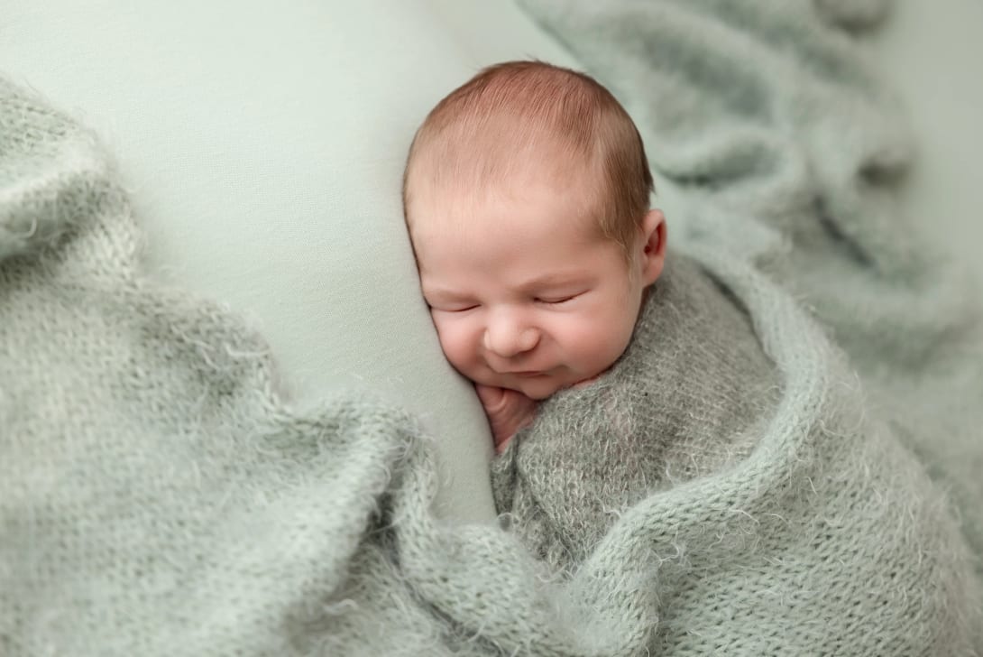A peaceful newborn baby swaddled in a white blanket, cradled gently in hands, showcasing newborn photography technique