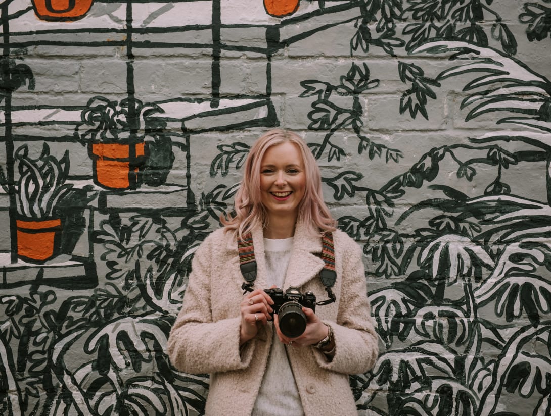 Portrait of Glasgow photographer Louise Mallan standing in front of a Glasgow city mural