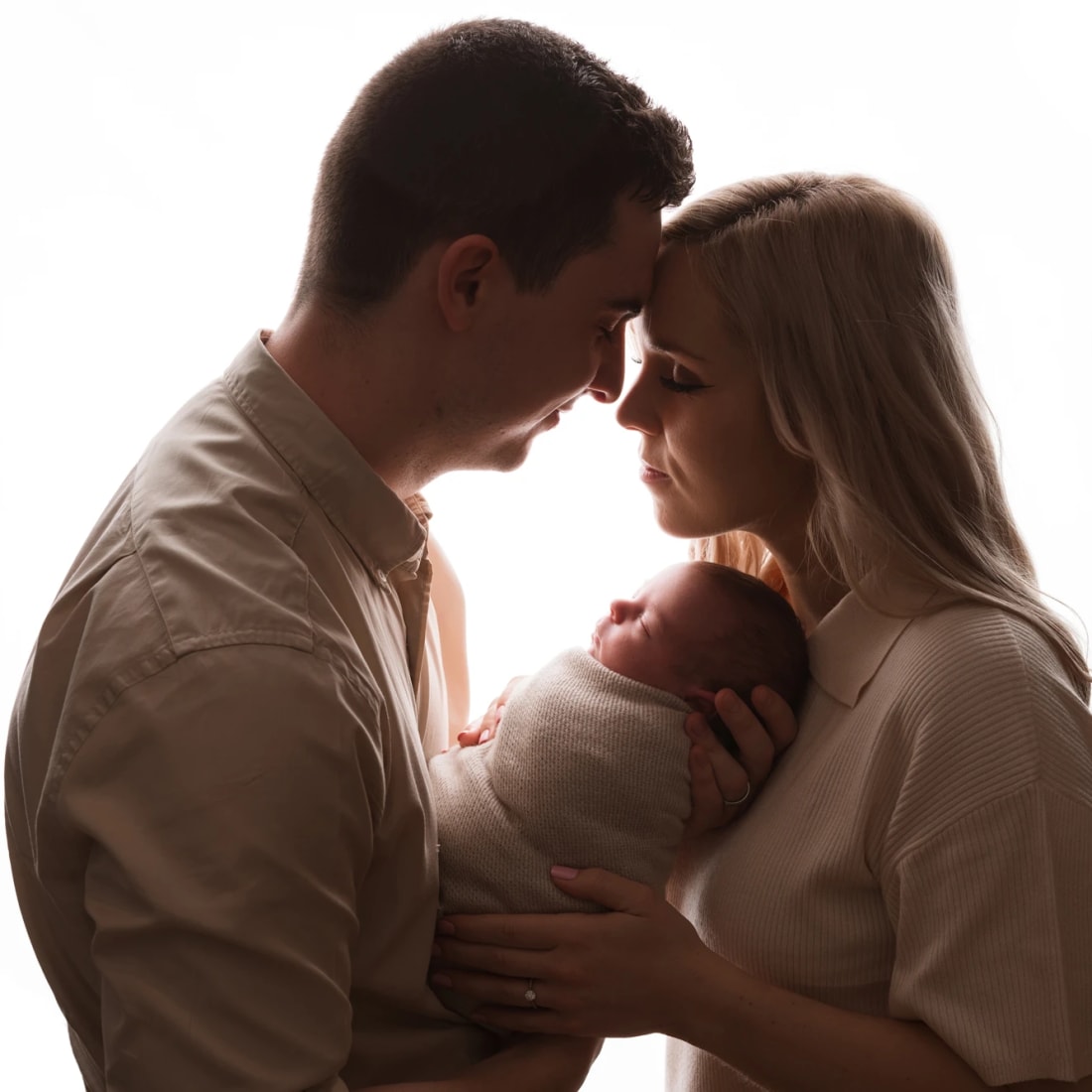 A tender moment in newborn photography with parents cradling their baby, captured in a soft backlight in Glasgow