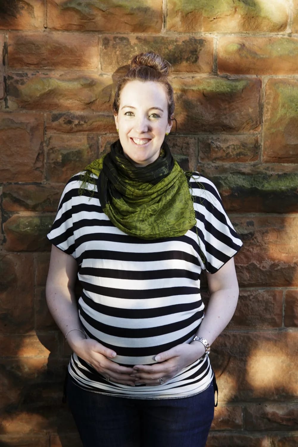 A pregnant woman in a striped shirt smiles warmly during a maternity session in Maxwell Park, Glasgow