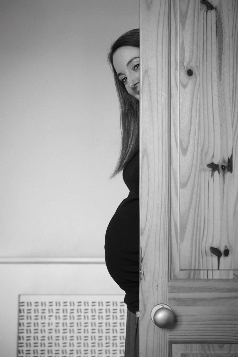 A pregnant woman playfully peeks from behind a door during a Maxwell Park maternity session in Rutherglen