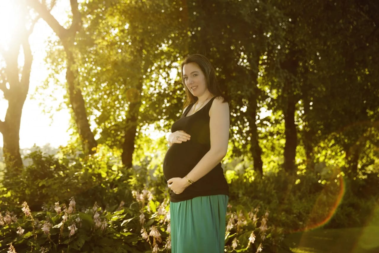 Pregnant woman in a green skirt poses in Maxwell Park during a maternity session, surrounded by lush greenery.