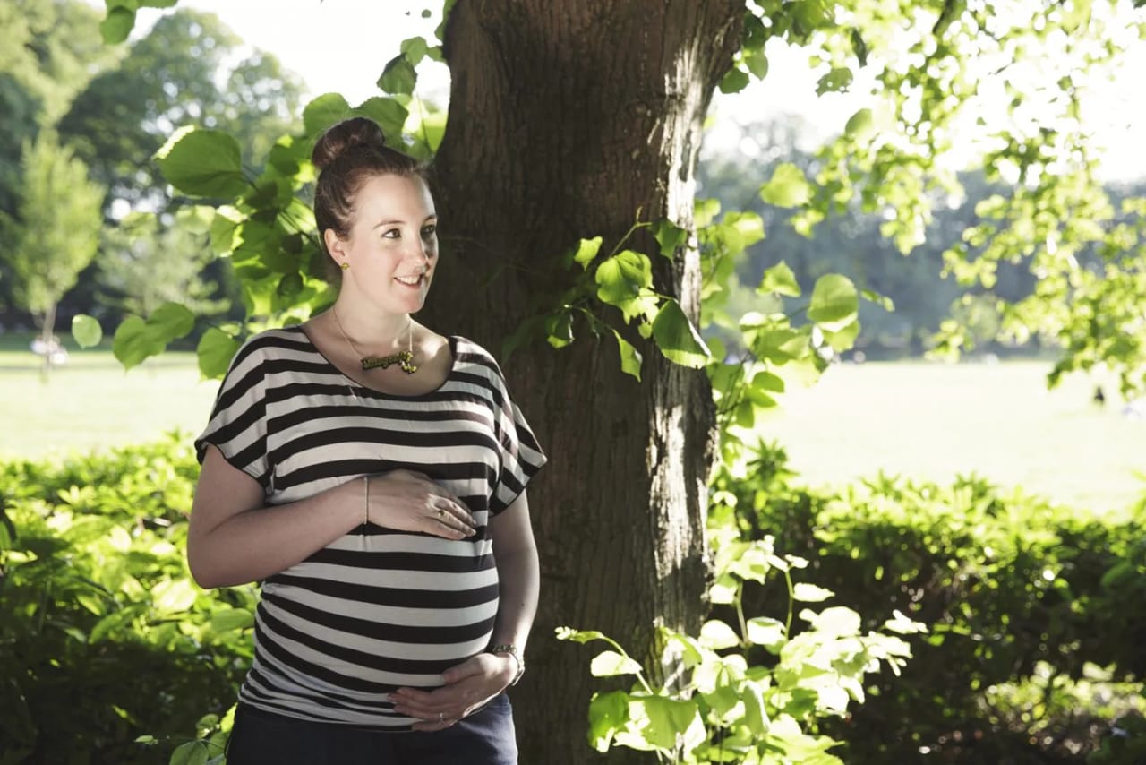 Pregnant woman in a striped shirt poses by a tree during a Maxwell Park maternity session
