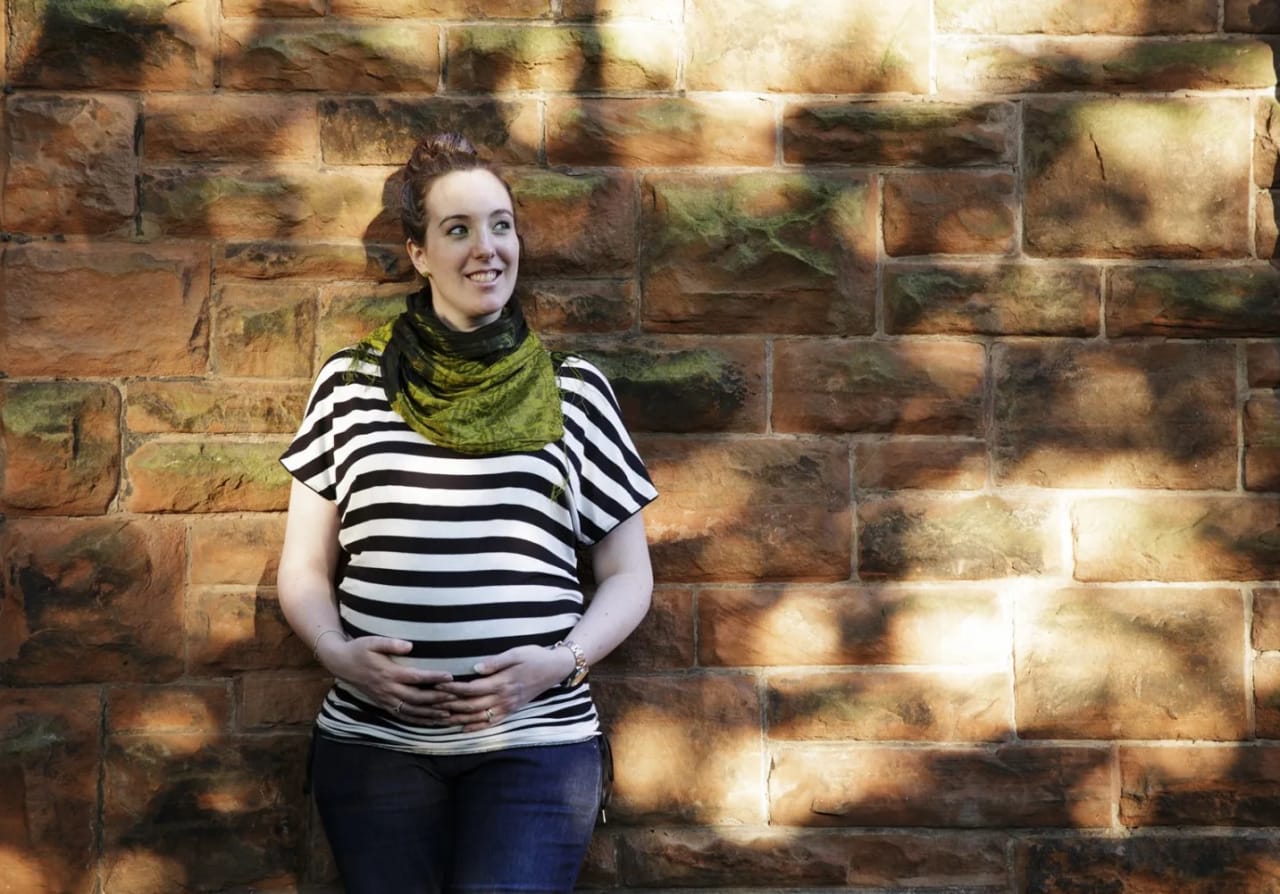 Prenant woman leaning against red stand stone wall with tree shadowing