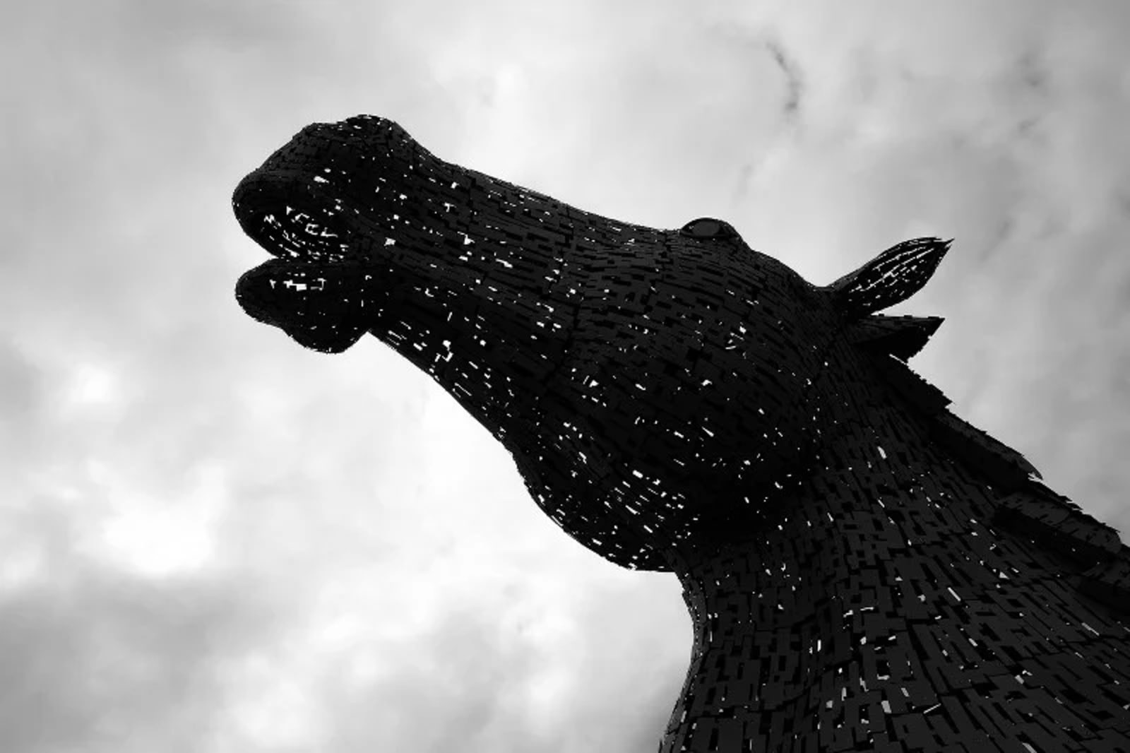 A striking view of a Kelpies monument sculpture against a cloudy sky, showcasing intricate metalwork detail