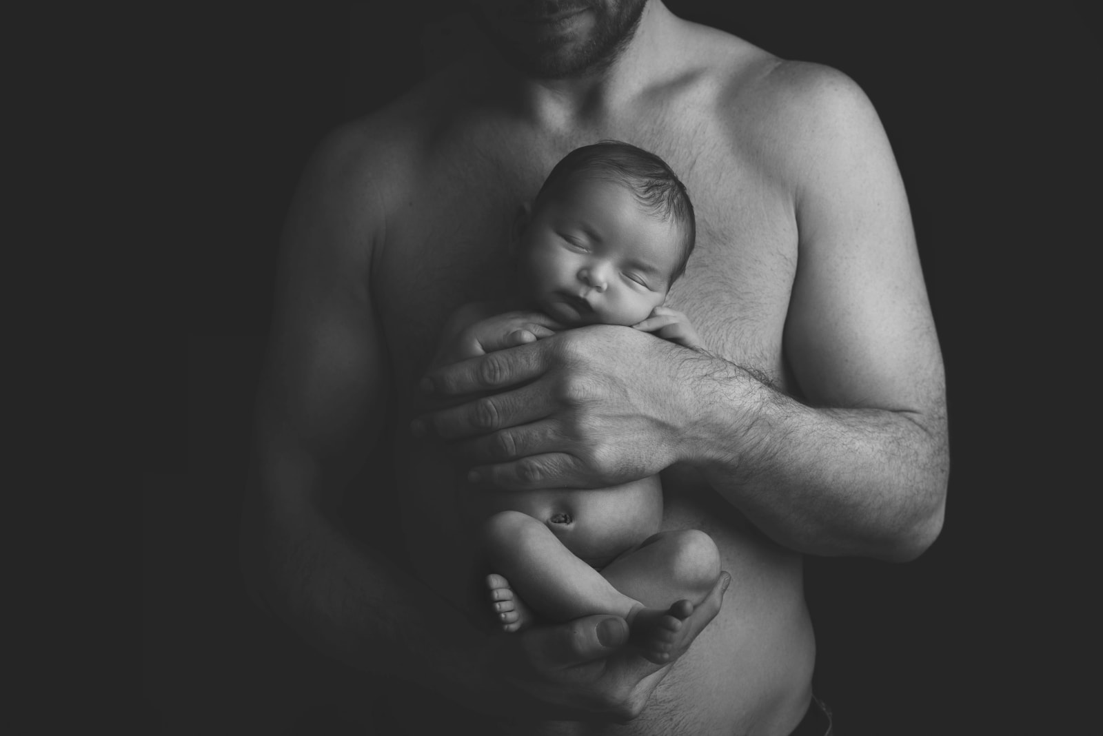 Black and white image of a father tenderly holding his newborn baby, showcasing intimate newborn photography in Drumsagard