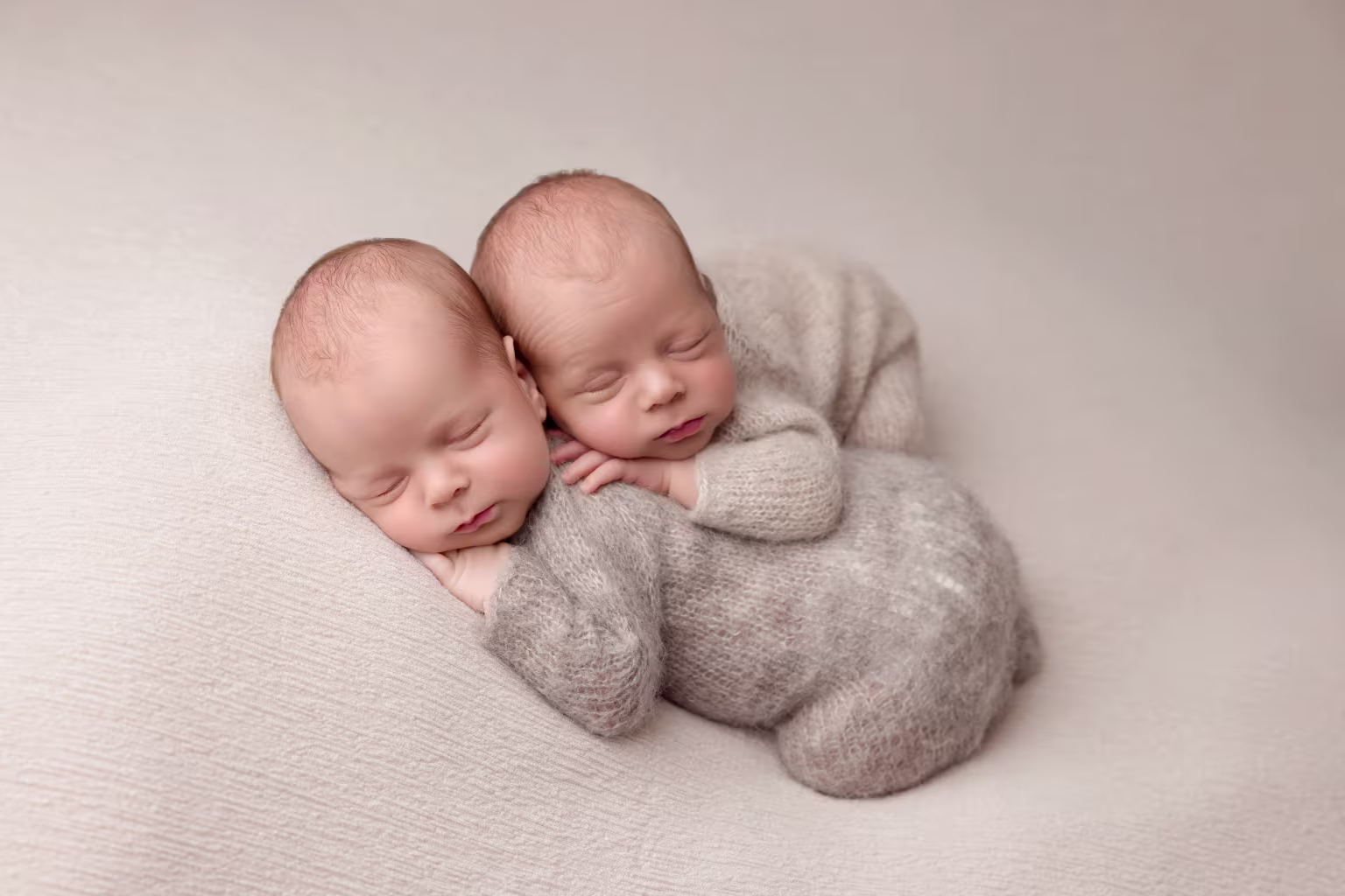 Twin newborns peacefully sleeping in cuddly gray outfits during a photography session in Newton