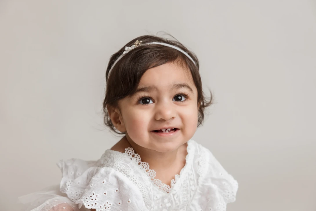 Smiling baby in a white dress posing for a baby photography session in Glasgow studio