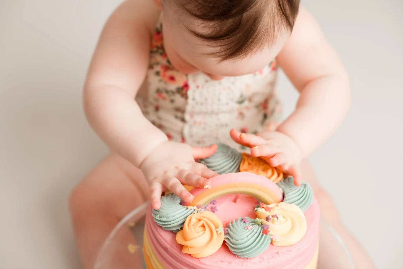 Baby enjoying cake smash with colorful icing and rainbow decoration in Newton