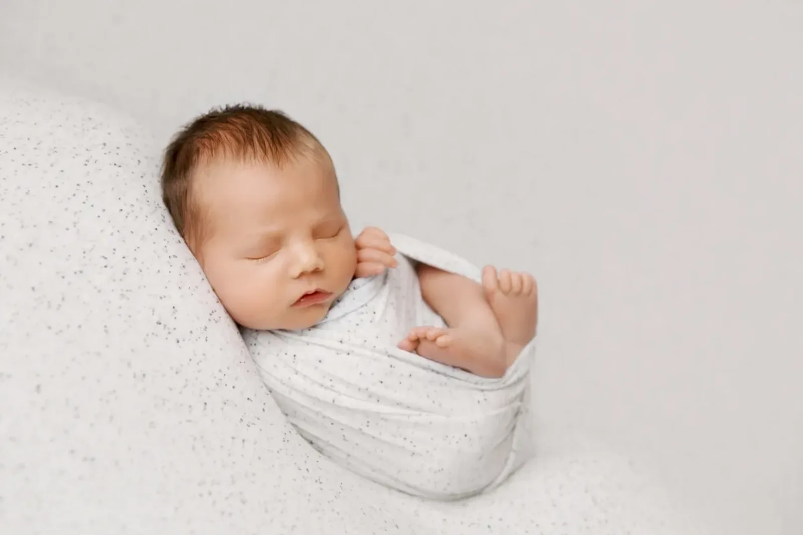 Peaceful newborn baby wrapped in a soft white blanket, showcasing tender moments in newborn photography in Drumsagard