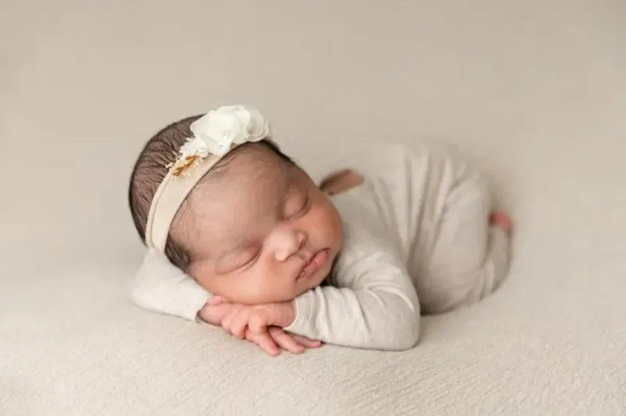 A peaceful newborn baby in a cozy outfit and headband sleeps on a soft blanket, showcasing adorable newborn photography style