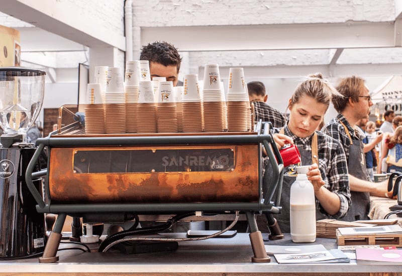 Baristas making coffee behind the espresso machine of a busy independent coffee shop