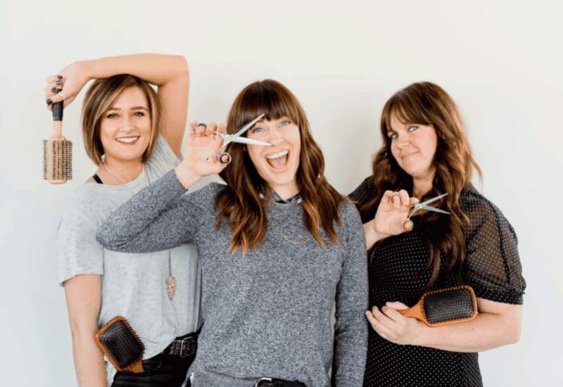 Three smiling hair stylists holding scissors and brushes in their salon