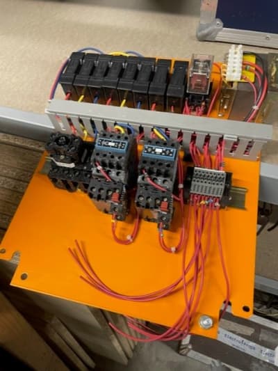 Electrical cabinet innards with fuse holders & circuit breakers mounted on orange metal plate