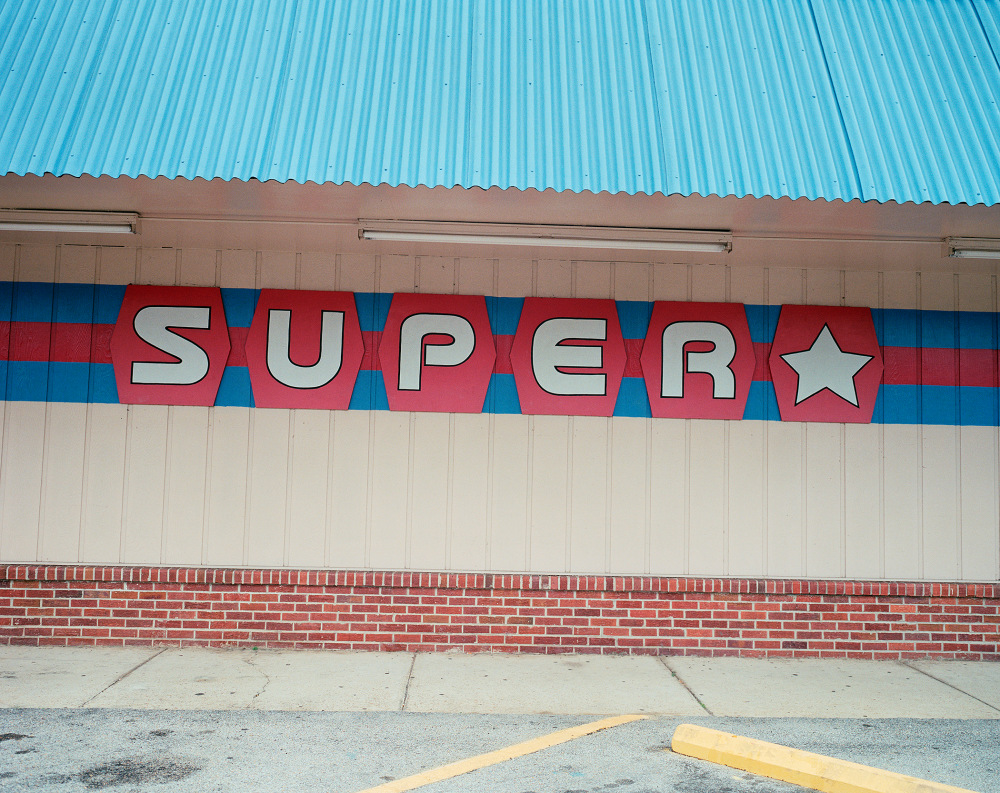 Colorful "SUPER" sign displayed on a building wall with a blue roof