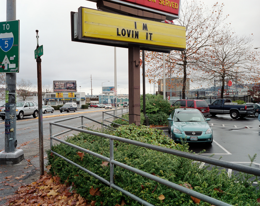 A street view of a parking lot with a sign displaying "I'M LOVIN IT" and trees in the background