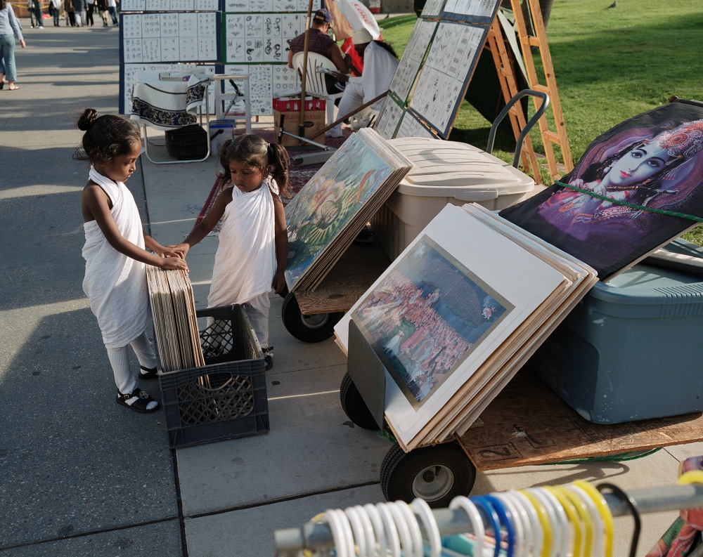 Two young girls dressed in white examine artwork at a street artist market
