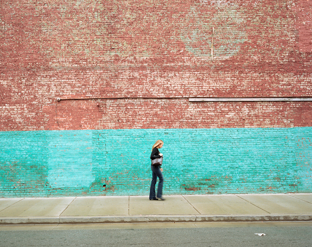 A woman walks past a textured red and teal brick wall