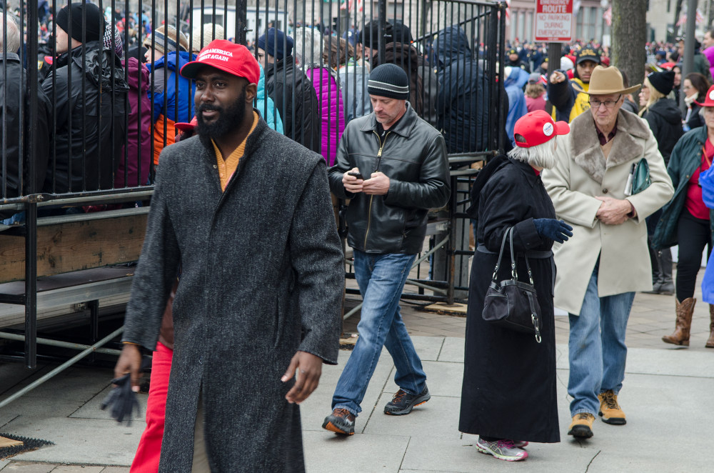A diverse group of people walking near a fenced area during a public event