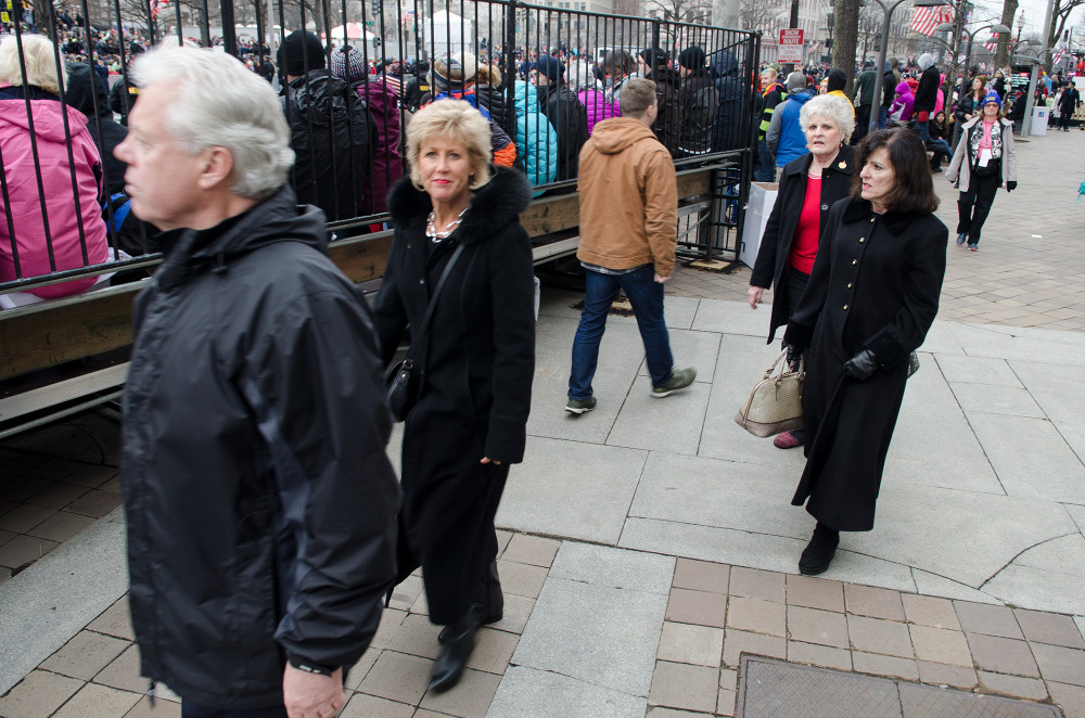 A group of people walking past a crowd gathered behind a fence at an outdoor event