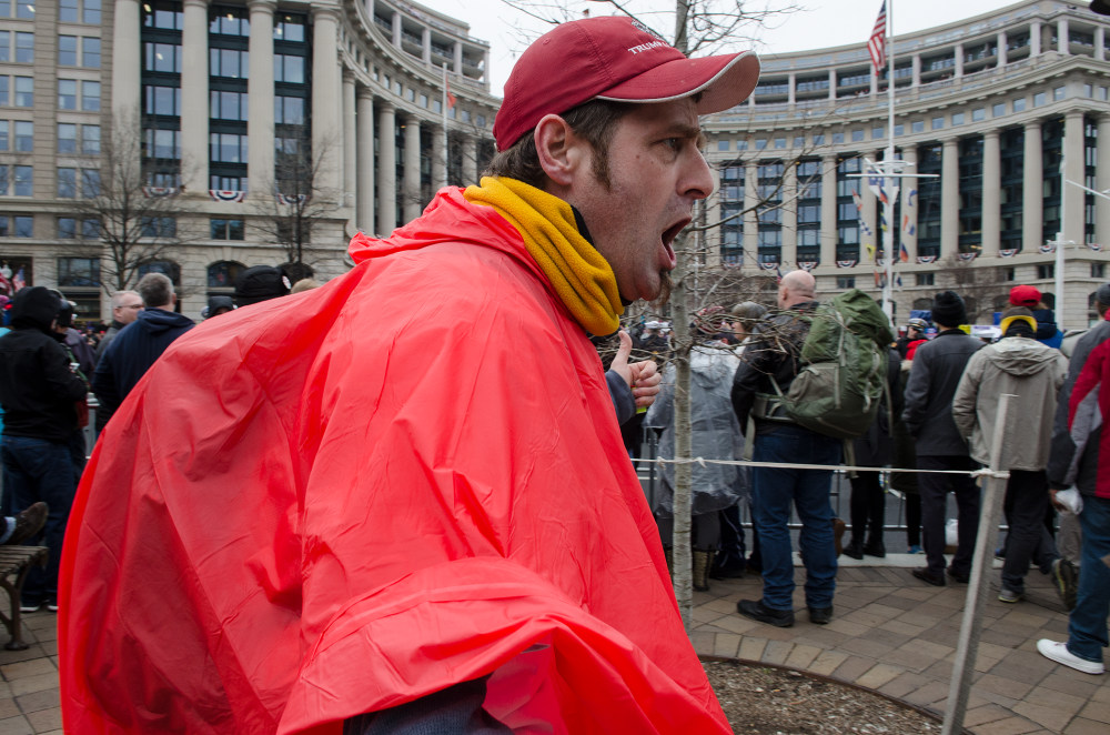 A man in a red poncho shouts at a crowded rally outside a government building