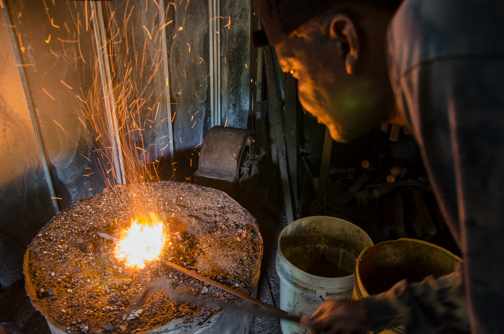 Blacksmith working with molten metal, creating sparks in a dimly lit workshop