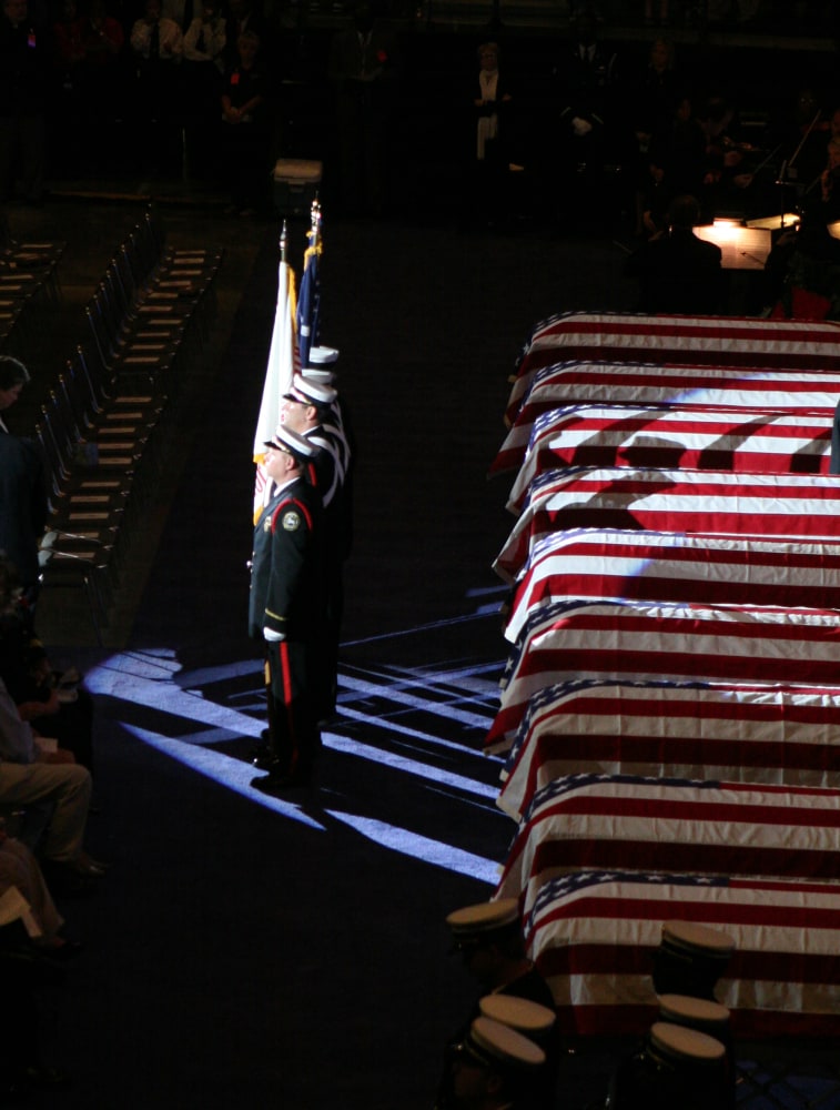 Military honor guard standing beside flag-draped caskets in a solemn setting