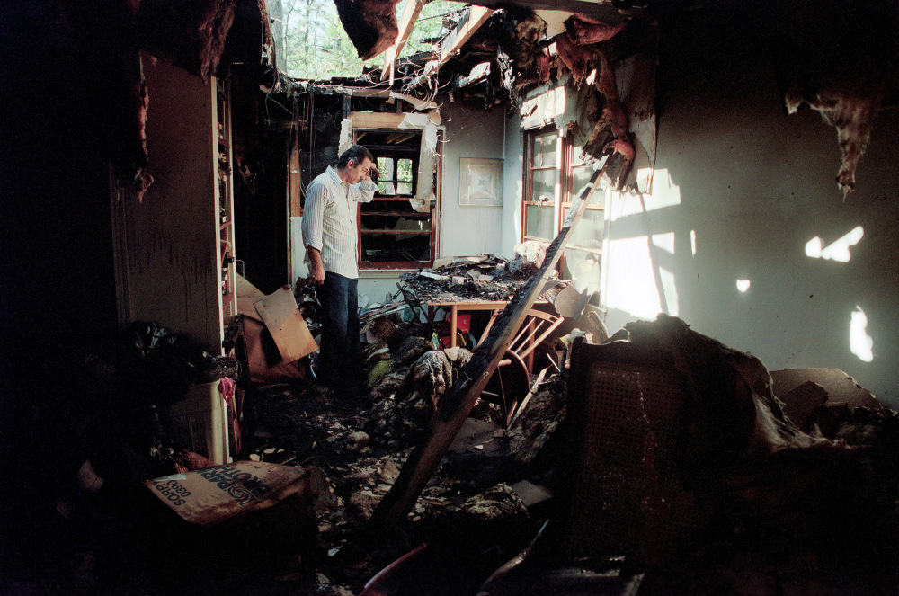 A person examines debris and damage in a burnt interior room