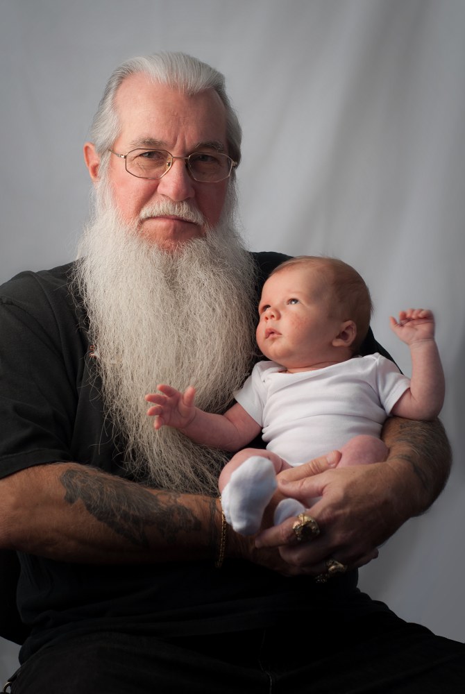 A bearded man holds a baby while gazing thoughtfully
