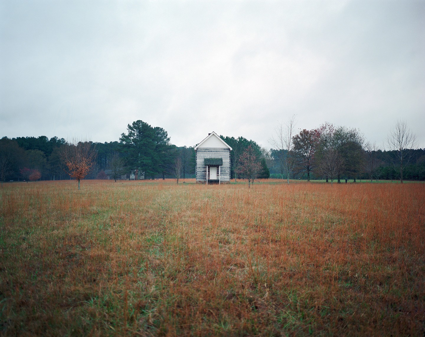 A solitary white house in a grassy field under a cloudy sky