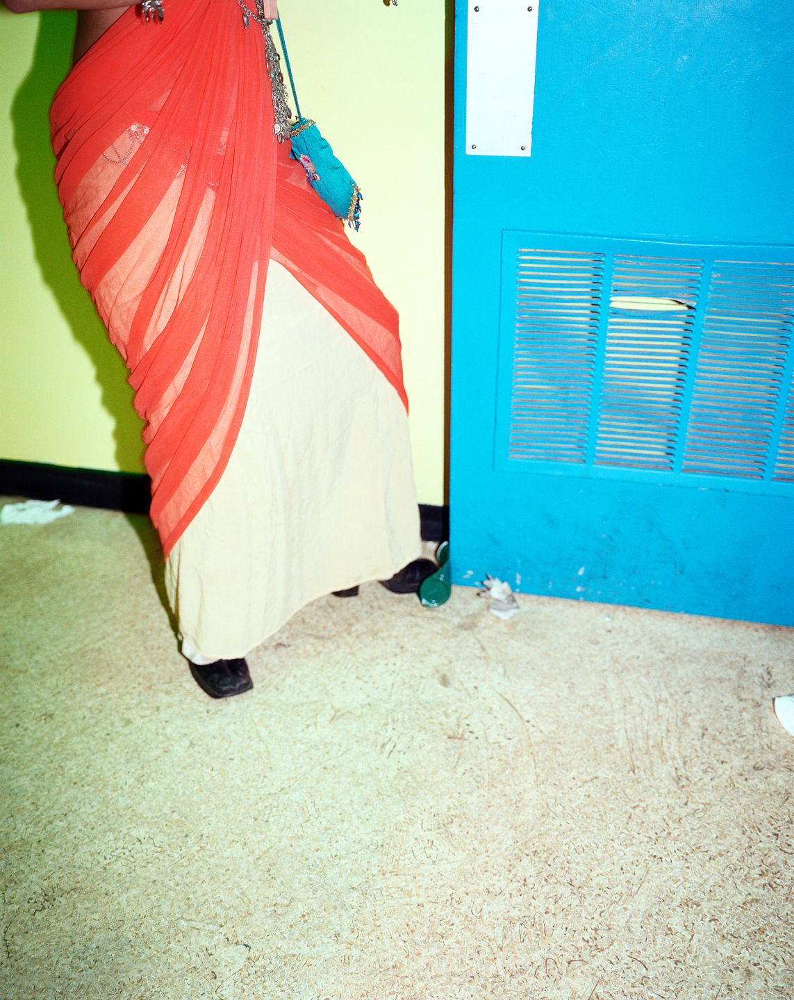 A person wearing a vibrant orange and beige outfit stands next to a blue door in a casual indoor setting