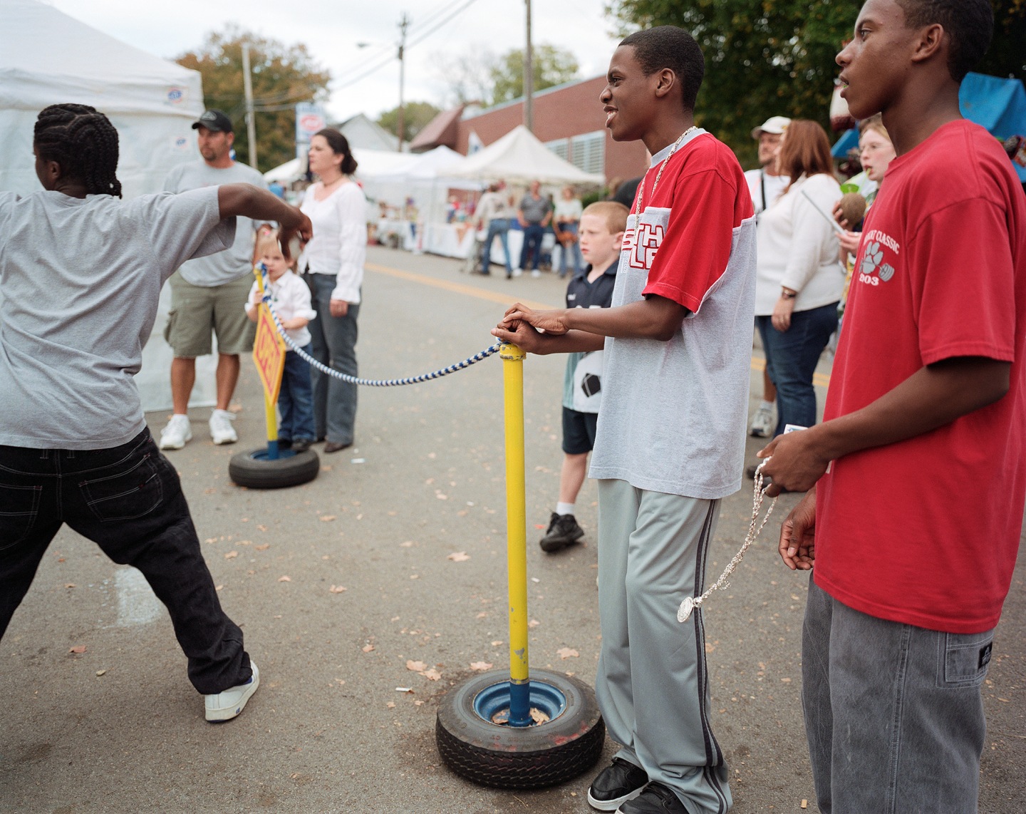 Two young men holding a tethered tire while children play at a fair