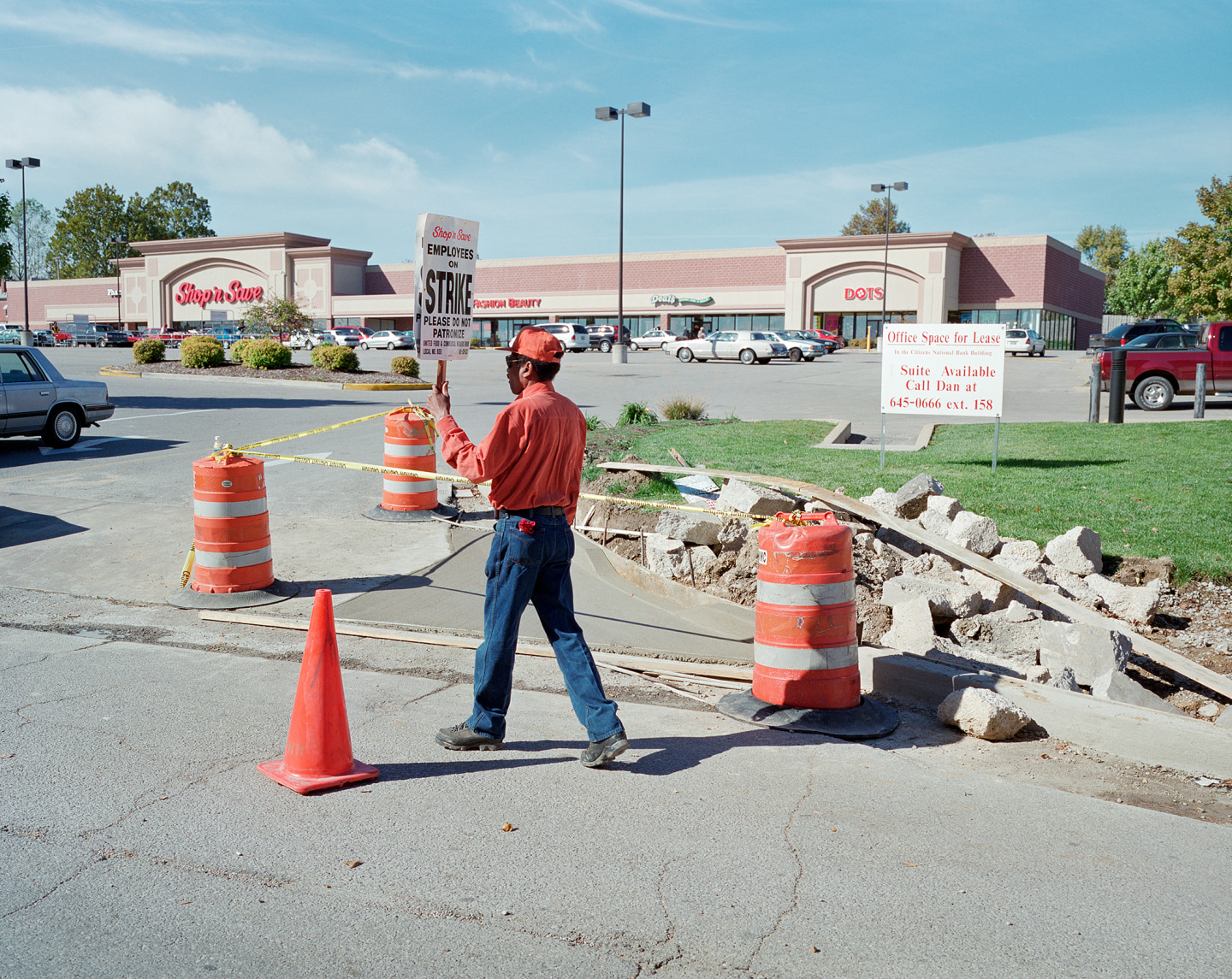 Worker holding a strike sign in a construction area with traffic cones and caution tape