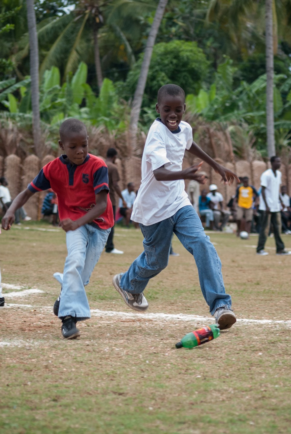 Two children running on a grassy field during a game, with spectators in the background