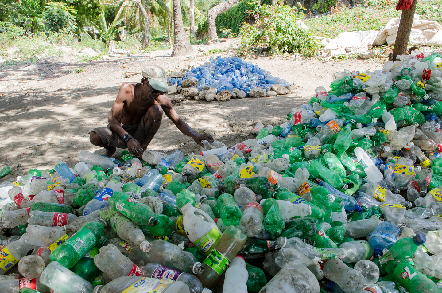 Man sorting through a large pile of plastic bottles in an outdoor setting