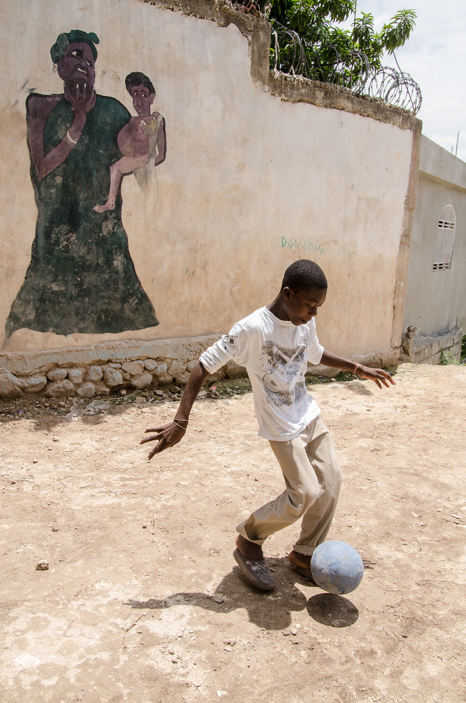 A young boy plays soccer in front of a mural depicting a woman with children